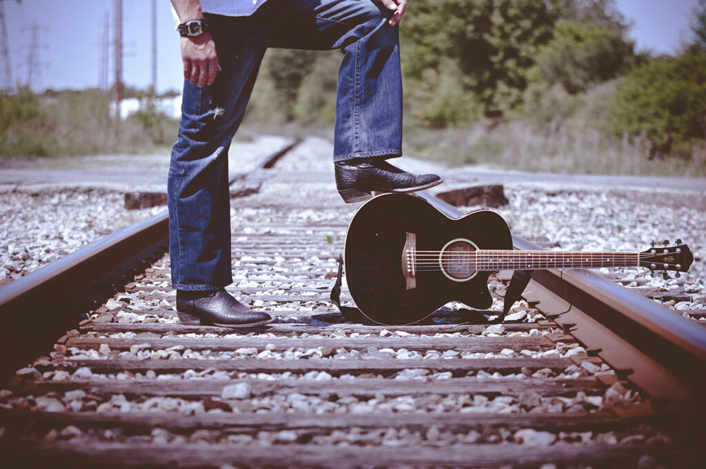 Man standing by train tracks with foot on guitar